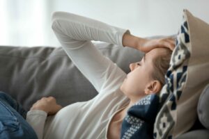 Une femme allongée sur un canapé se tient la tête à cause d'un mal de tête