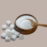 A wooden bowl filled with sugar and wooden spoon on brown background and sugar cubes next to it.