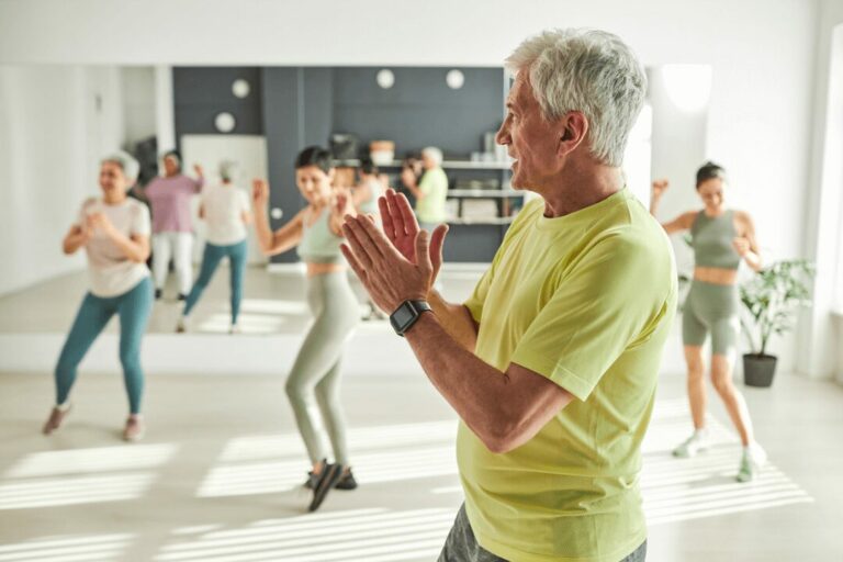 Un homme se tient au premier plan en applaudissant. En arrière-plan, d'autres femmes et hommes font du sport.