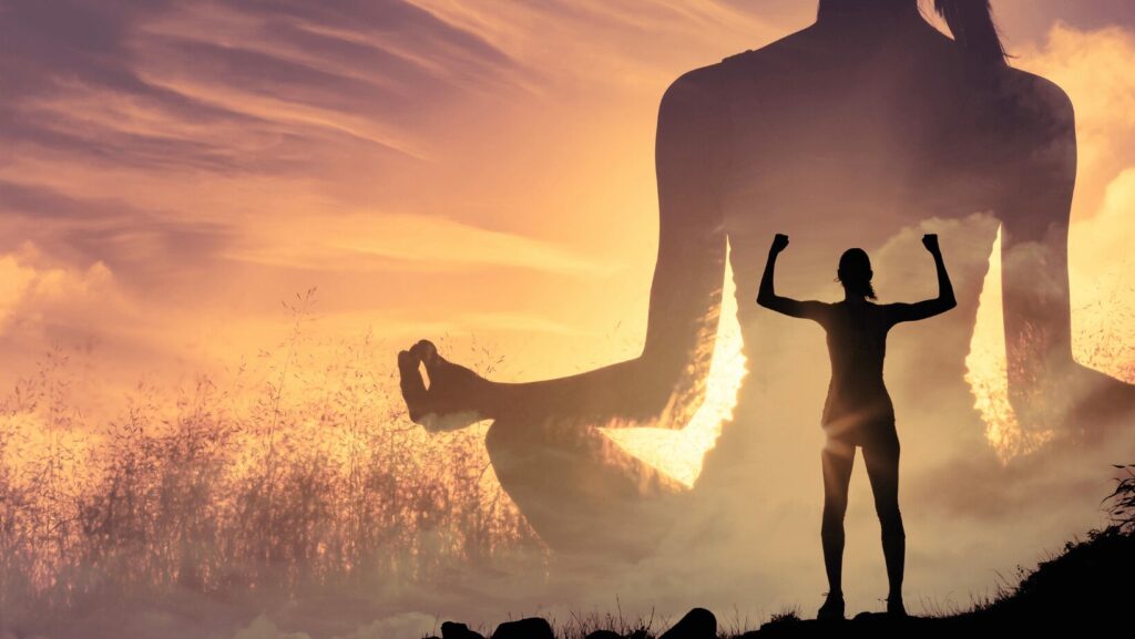 femme forte au coucher du soleil dans un champ, les deux bras en l'air, et derrière elle, une ombre géante d'elle-même dans une position de yoga