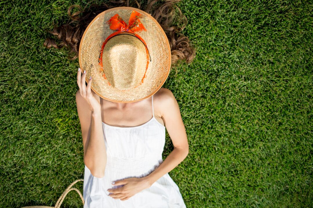 Donna sdraiata su un prato con un cappello sul viso che prende il sole. Evitare l'allergia al sole