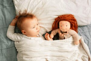 Il bambino è sdraiato nel letto con accanto una bambola. Entrambi hanno piccole macchie rosse sul viso, che mostrano l'eruzione cutanea della varicella.