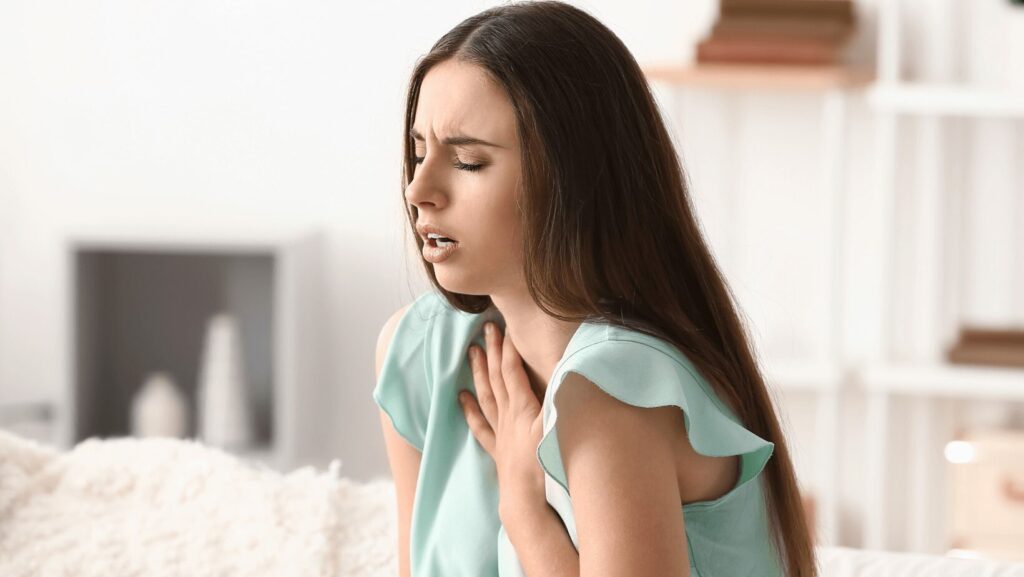 joven de pelo castaño y camisa turquesa sufre un ataque de asma en el salón de su casa