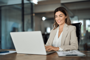 Une femme souriante assise à son poste de travail devant son ordinateur portable