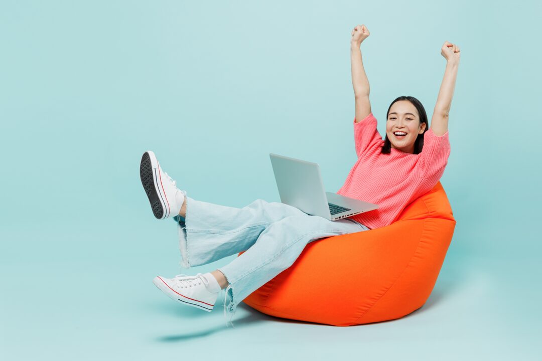 Frau sitzt lachend auf einem Sessel vor ihrem Laptop