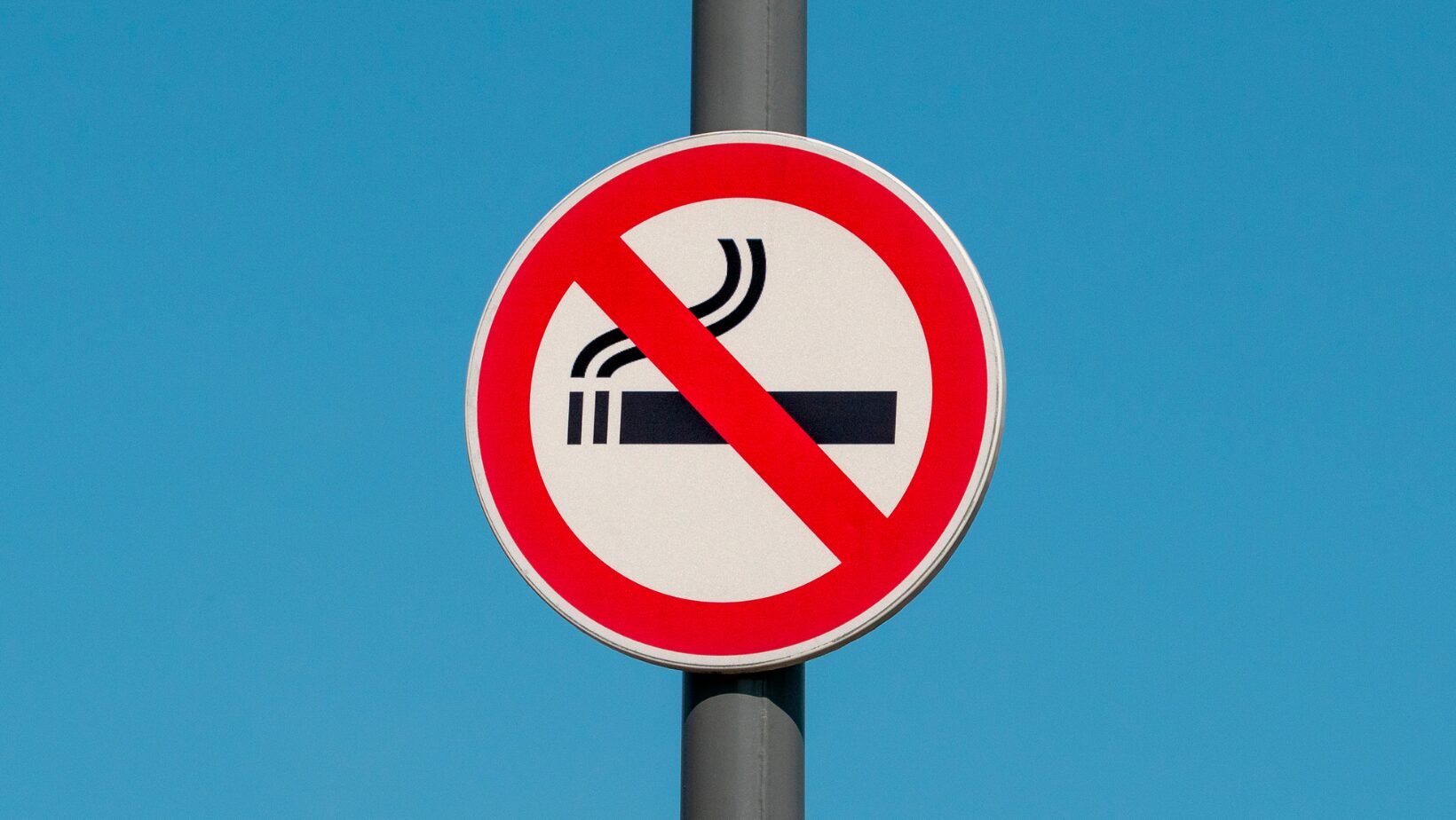 cartello rosso e bianco con una sigaretta nera barrata su sfondo blu