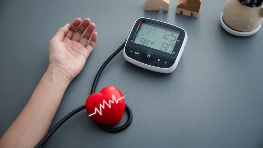 bras et main reliés à un tensiomètre et à côté un cœur rouge pour montrer qu'il s'agit de la pression artérielle