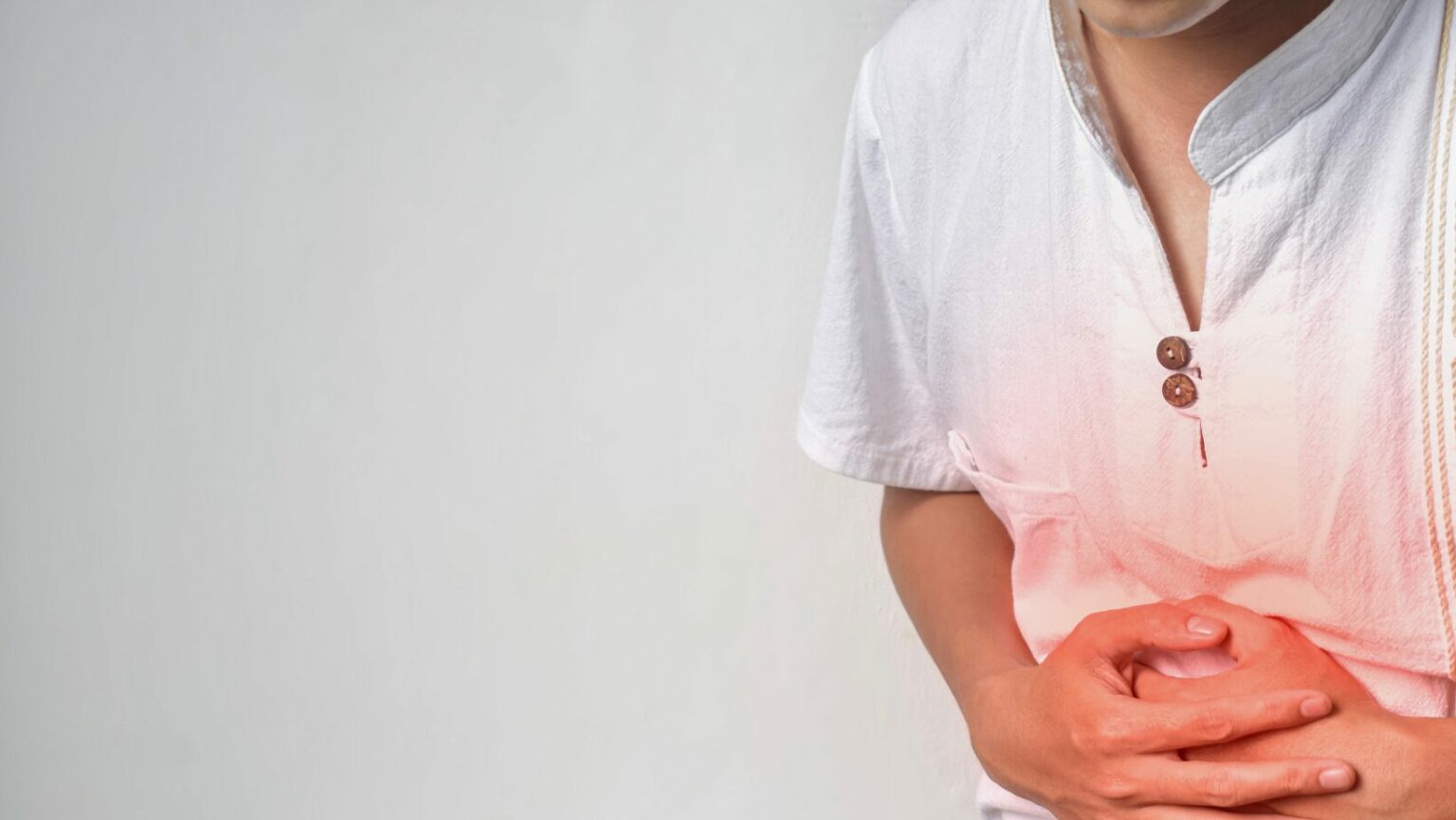 man with a white shirt on a gray background holding his hands to his belly because of irritable bowel syndrome and the area glows red