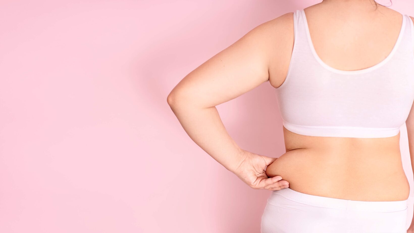 woman in pink underwear in front of a pink background holding her hand to her side belly